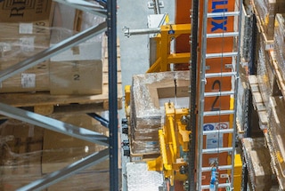 The stacker crane moves along the aisle to retrieve a pallet from another location